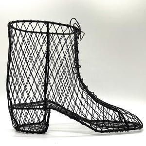 Puede incluir: Cesta en forma de bota de alambre negro. La cesta está construida con una serie de alambres que se cruzan, formando un patrón de diamantes. La bota tiene tacón y cordones. El diseño general es abierto y aireado, adecuado para almacenamiento decorativo.