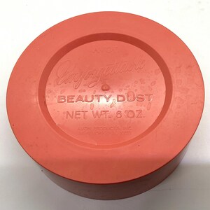 May include: A round, orange plastic container with a white label that reads "Avon Unforgettable Beauty Dust Net Wt. 6 oz. Avon Products Inc. New York, NY 10020."