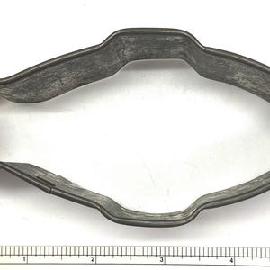 May include: A vintage metal cookie cutter shaped like a fish. The cutter is made of dark gray metal and has a slightly worn appearance.