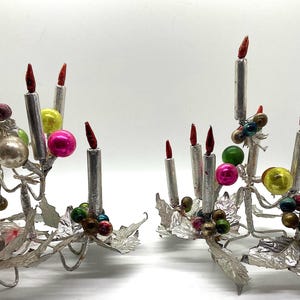 May include: Two silver candle holders with red candles and colourful glass baubles. The holders are decorated with silver leaves and are ideal for a vintage Christmas decoration.