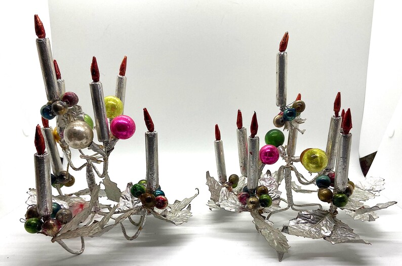 May include: Two silver candle holders with red candles and colourful glass baubles. The holders are decorated with silver leaves and are ideal for a vintage Christmas decoration.
