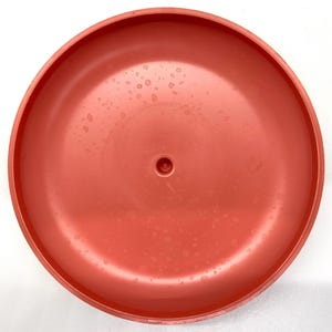 May include: A bright orange plastic disc with a small hole in the center. The disc has a smooth, glossy finish and is covered in small water droplets.