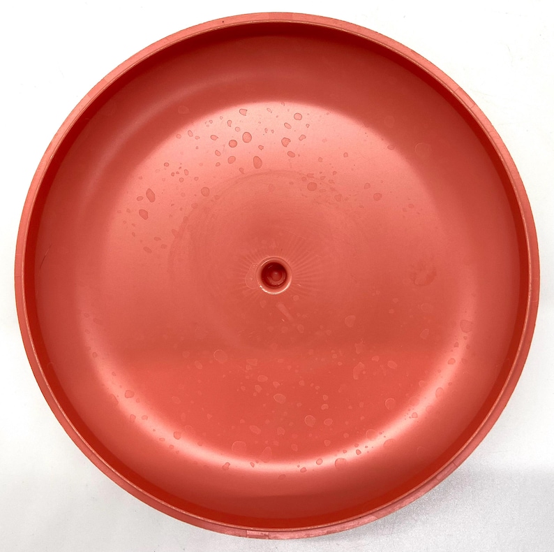 May include: A bright orange plastic disc with a small hole in the center. The disc has a smooth, glossy finish and is covered in small water droplets.