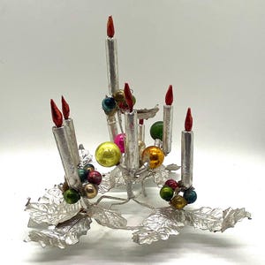 May include: Silver Christmas tree topper with a candelabra design featuring six silver candles with red flames and a base of silver holly leaves with colourful glass baubles.