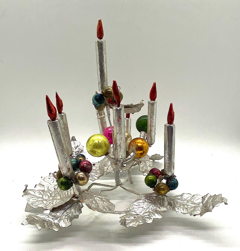 May include: Silver Christmas tree topper with a candelabra design featuring six silver candles with red flames and a base of silver holly leaves with colourful glass baubles.