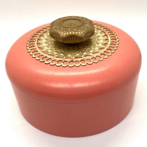 May include: A vintage pink round trinket box with a gold filigree lid and a gold knob.