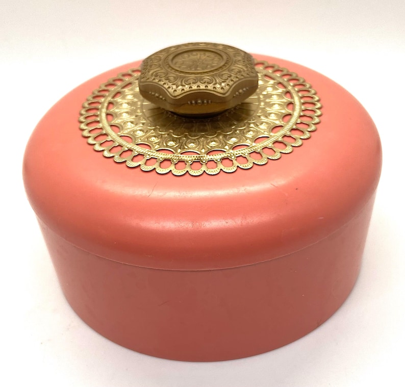 May include: A vintage pink round trinket box with a gold filigree lid and a gold knob.