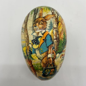 May include: A vintage Easter egg made of paper mache with a colorful illustration of a rabbit wearing a blue jacket and holding a purse. The rabbit is standing in a forest setting.