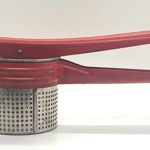 Puede incluir: Un pasapurés de metal rojo con un colador de malla de acero inoxidable. El pasapurés tiene un mango que se utiliza para presionar las patatas a través del colador.