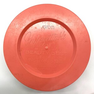 May include: A bright orange plastic lid with the text "Avon Unforgettable Beauty Dust Net Wt. 6 oz. Avon Products Inc. New York NY, 10020" printed on it.