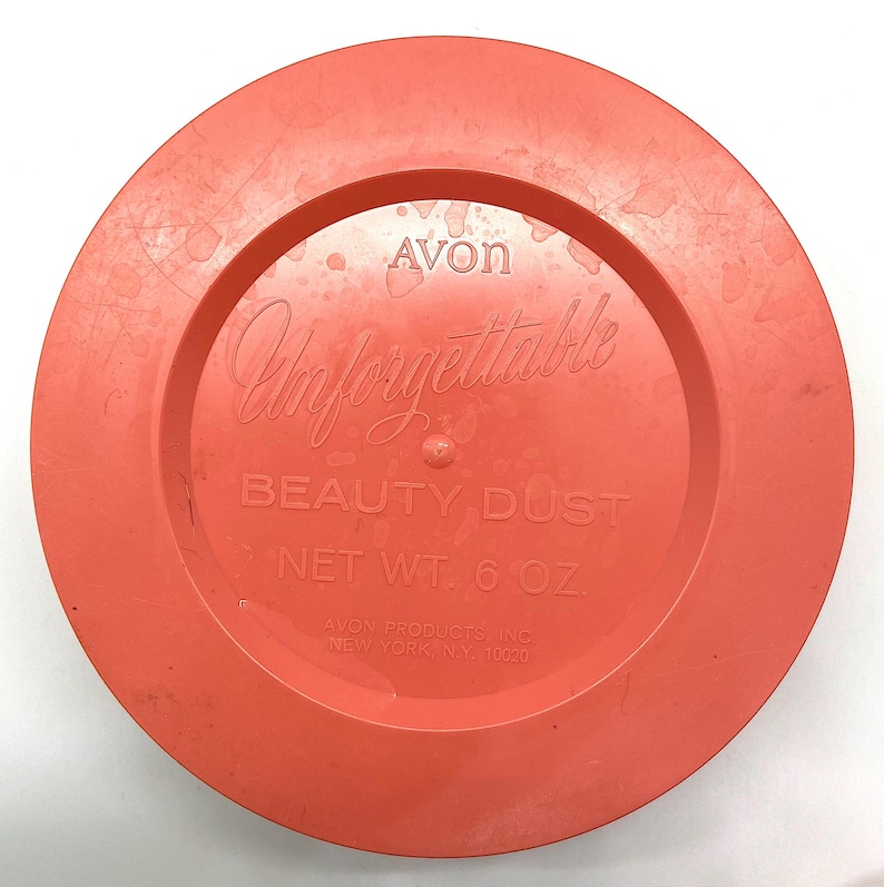 May include: A bright orange plastic lid with the text "Avon Unforgettable Beauty Dust Net Wt. 6 oz. Avon Products Inc. New York NY, 10020" printed on it.
