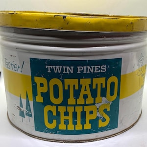 Puede incluir: Una lata de metal vintage para patatas fritas. La lata es blanca con una tapa amarilla y una etiqueta azul y amarilla que dice "Twin Pines Potato Chips" con dos pinos en el lado izquierdo de la etiqueta. El texto "Tastier!" está impreso en amarillo en el lado izquierdo de la lata.