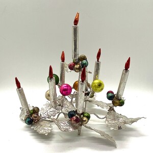 May include: Silver Christmas tree centrepiece with seven silver candles and colourful glass baubles. The base of the tree is made of silver leaves.