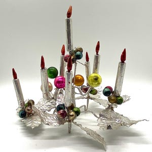 May include: Silver Christmas tree centrepiece with seven silver candles and colourful glass baubles. The base of the centrepiece is made of silver leaves.
