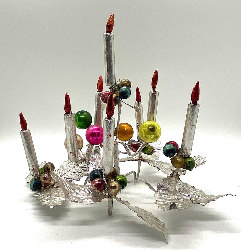 May include: Silver Christmas tree centrepiece with seven silver candles and colourful glass baubles. The base of the centrepiece is made of silver leaves.
