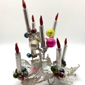 May include: A silver metal Christmas tree decoration with a candelabra design. The ornament features seven silver candles with red tips, and is decorated with colourful glass beads.