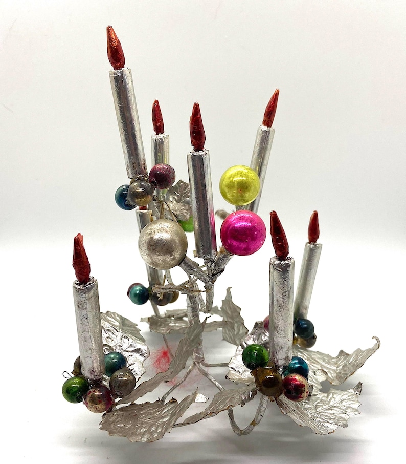 May include: A silver metal Christmas tree decoration with a candelabra design. The ornament features seven silver candles with red tips, and is decorated with colourful glass beads.