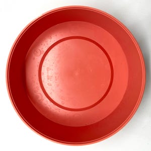 May include: A bright orange plastic planter pot with a smooth, slightly textured surface. The pot is round and has a wide opening.