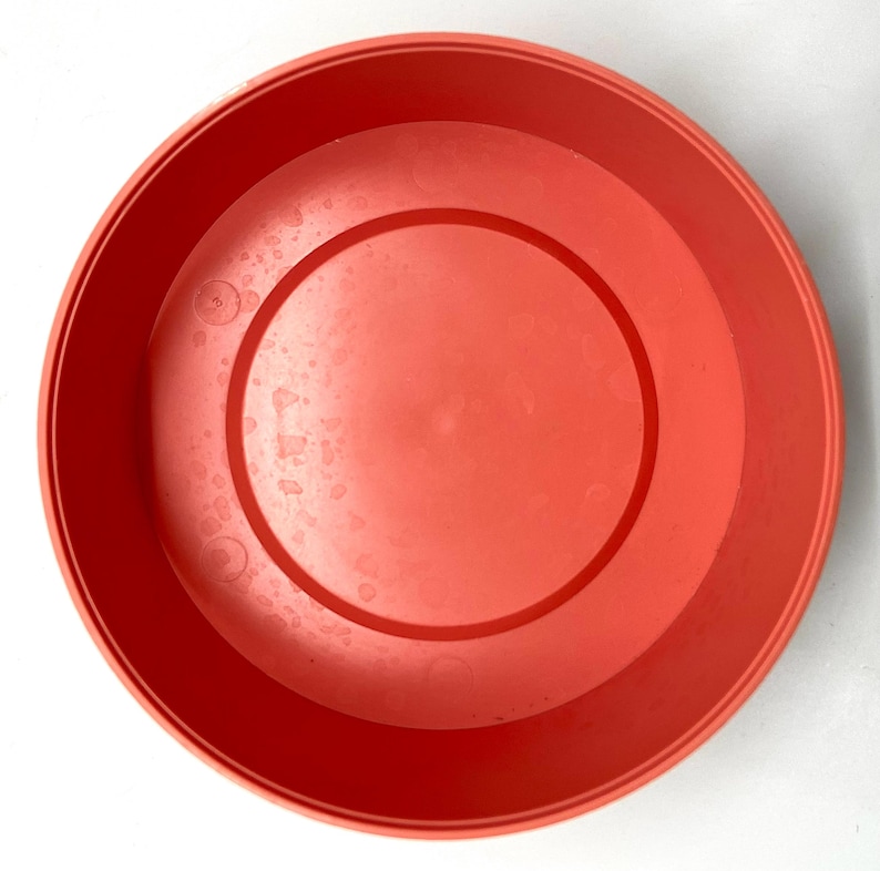 May include: A bright orange plastic planter pot with a smooth, slightly textured surface. The pot is round and has a wide opening.