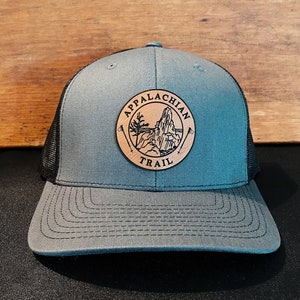 May include: A gray and black trucker hat with a brown leather patch that says "Appalachian Trail" and features a mountain silhouette.
