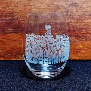 May include: A clear glass wine glass with an etched design of a mountain range. The glass is sitting on a dark surface.