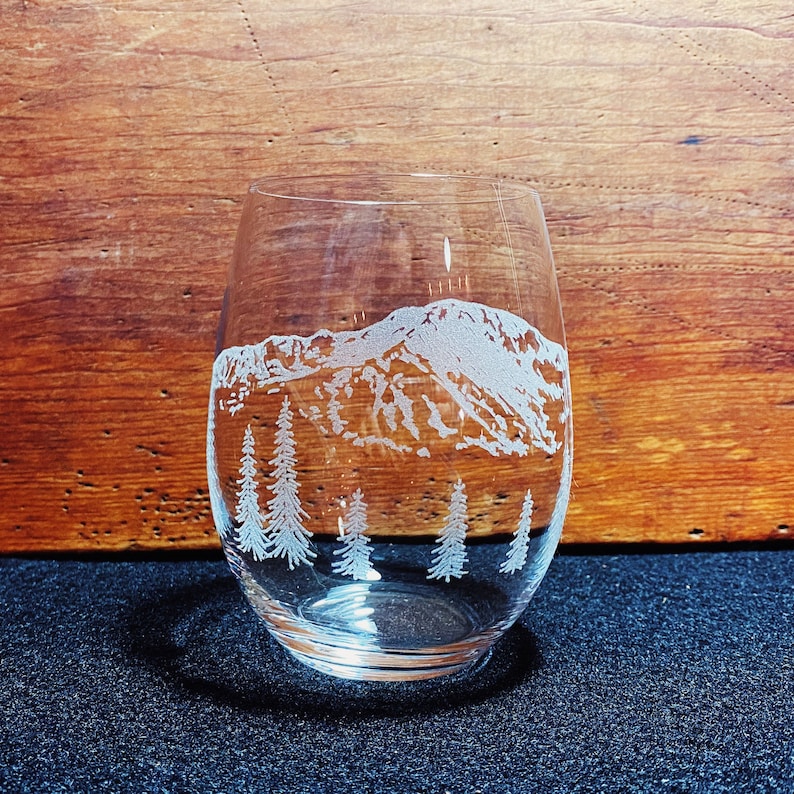 Puede incluir: Una copa de vino de vidrio transparente con un dise&ntilde;o grabado de una cordillera y pinos.