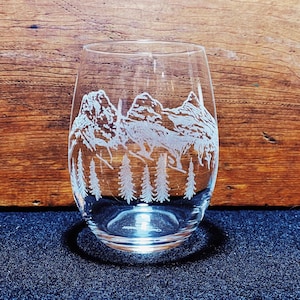 May include: A clear glass wine glass with an etched design of a mountain range and pine trees.