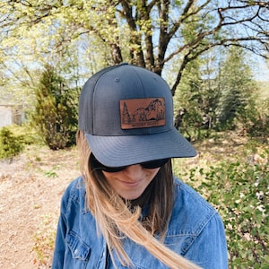 May include: A black and brown trucker hat with a brown leather patch featuring a mountain range and the text "Mount Shasta".