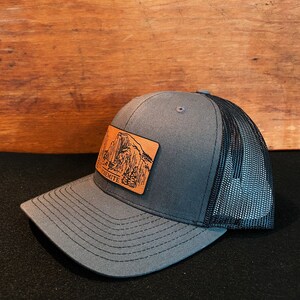 May include: A gray and black trucker hat with a brown leather patch featuring a mountain range and the word "Yosemite".