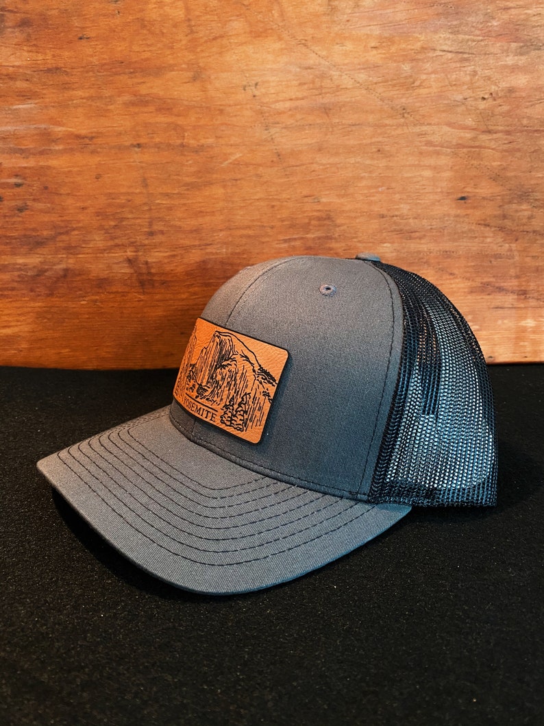 May include: A gray and black trucker hat with a brown leather patch featuring a mountain range and the word "Yosemite".