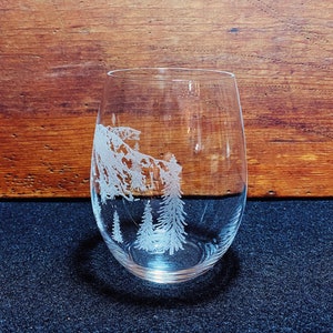 Puede incluir: Una copa de vino de vidrio transparente con un dise&ntilde;o grabado de una cordillera y &aacute;rboles. La copa est&aacute; vac&iacute;a y se encuentra sobre una superficie oscura.