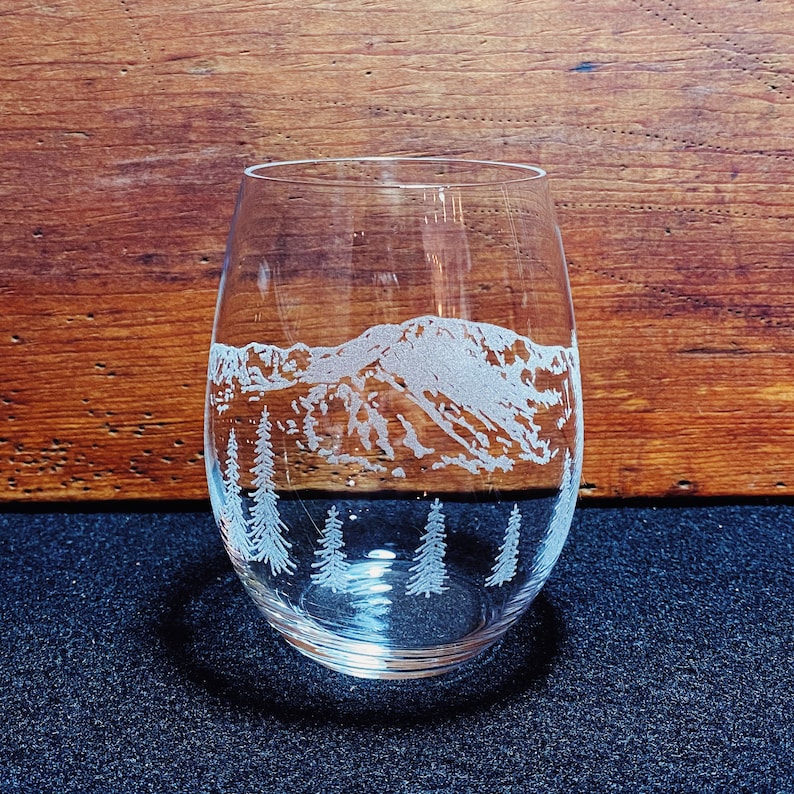 Puede incluir: Una copa de vino de vidrio transparente con un dise&ntilde;o grabado de una cordillera y pinos.