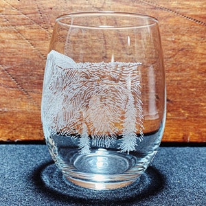 May include: A clear glass wine glass with an etched design of a forest scene. The design features trees and a mountain in the background.