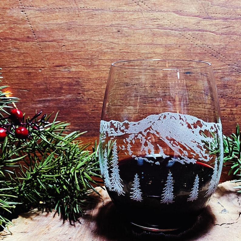 Puede incluir: Una copa de vino de vidrio transparente con una cordillera y &aacute;rboles grabados en el lateral. La copa est&aacute; llena de vino tinto.