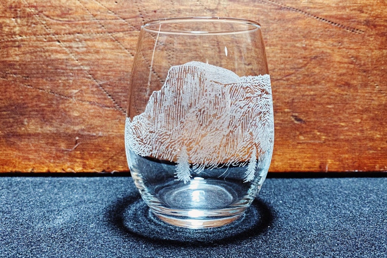 May include: A clear glass wine glass with an etched design of a mountain range. The glass is sitting on a dark surface.