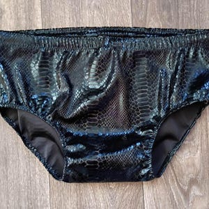 Op de afbeelding: Zwarte onderbroek met een slangenprint. De elastische tailleband is zichtbaar. Het materiaal heeft een glanzende, getextureerde uitstraling. De onderbroek is gemaakt van synthetisch materiaal.