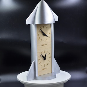 May include: A set of three ceramic mugs with a speckled, matte finish. The mugs are in shades of cream, light gray, and dark gray. Each mug has a simple, minimalist design and a rounded handle.