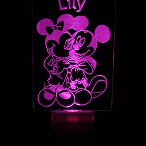 May include: A pink night light featuring a cartoon image of Mickey and Minnie Mouse embracing. The name "Lily" is displayed at the top. The night light is illuminated with a soft pink glow, perfect for a child's room.