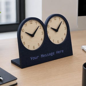 May include: A dual-dial desk clock featuring a dark blue frame with two circular light-colored wooden clock faces, black hands, and black numerals. The base of the frame includes the text Your Message Here in a light blue font color.