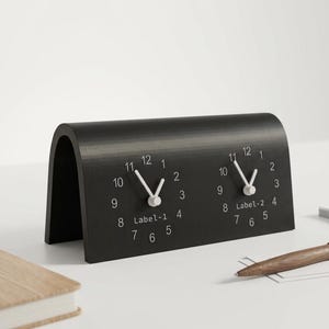 Puede incluir: Un reloj de escritorio negro en forma de arco con dos esferas analógicas circulares que tienen manecillas y números blancos. La esfera izquierda está etiquetada como Label-1 y la derecha como Label-2. El reloj tiene un acabado mate y liso.
