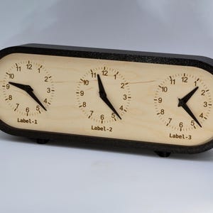 May include: A wooden clock with three separate clock faces, each with black hands and black Roman numeral markings. The clock faces are labeled "Label-1", "Label-2", and "Label-3".