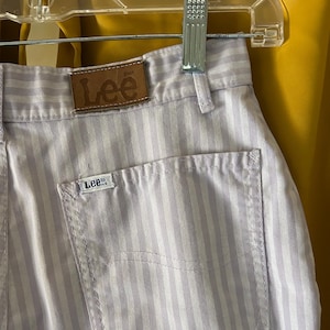 May include: Close-up of light purple and white striped Lee jeans. The jeans have a back pocket and a brown leather Lee label on the waistband. A small Lee label is on the back pocket.