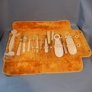May include: A vintage set of manicure tools in a rolled-up orange velvet case. The tools are made of ivory and include a cuticle pusher, nail clippers, tweezers, and a file.
