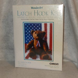 May include: A WonderArt Latch Hook Kit featuring an "All American Bear" design. The kit's packaging displays a brown teddy bear against a backdrop of the American flag. The approximate size of the finished project is 20" x 27".