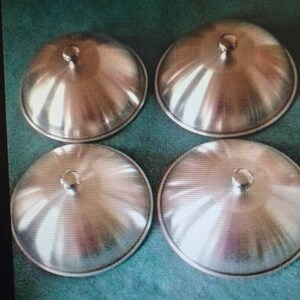 May include: Four silver metal lids for a pot or pan. The lids are round and have a small knob on top.