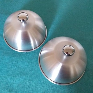 May include: Two silver metal dome-shaped serving dishes with shiny chrome handles.