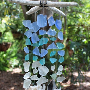 May include: A white starfish wind chime with blue and clear glass pieces and seashells hanging from it. The wind chime is hanging from a tree branch.