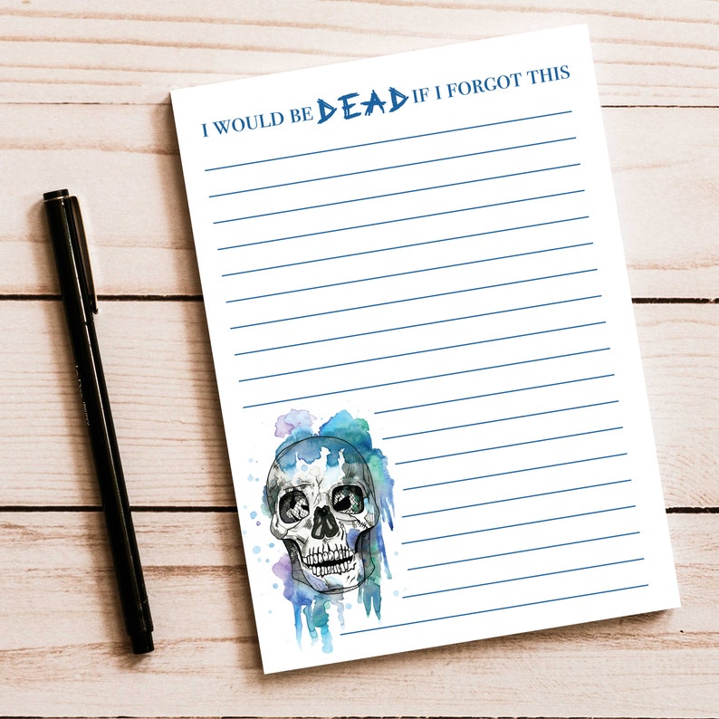 Op de afbeelding: Een gelijnd notitieblok met de blauwe tekst "I WOULD BE DEAD IF I FORGOT THIS". Een aquarel schedelontwerp staat onderaan. Een zwarte pen ligt op het houten oppervlak naast het notitieblok.