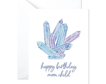 May include: A greeting card with a watercolor illustration of blue and purple crystals. The text on the card reads "happy birthday, moon child."