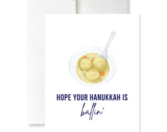 May include: A white card with a blue illustration of a bowl of matzah ball soup and the text "HOPE YOUR HANUKKAH IS ballin'" in blue.